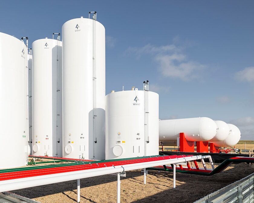 Large white vertical storage tanks with red-and-white piping at a bulk plant. 