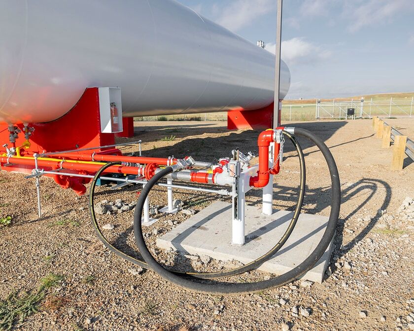 Close-up of piping and hose connections at the base of a large horizontal storage tank.