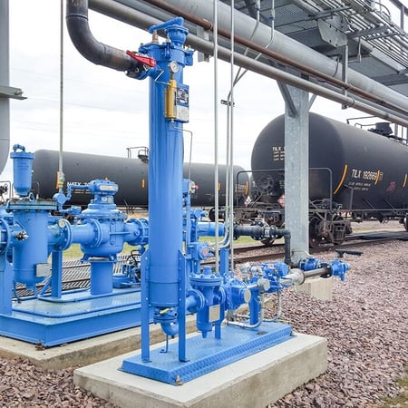 Blue blending skid at a rail terminal, with tank railcars on the tracks in the background.