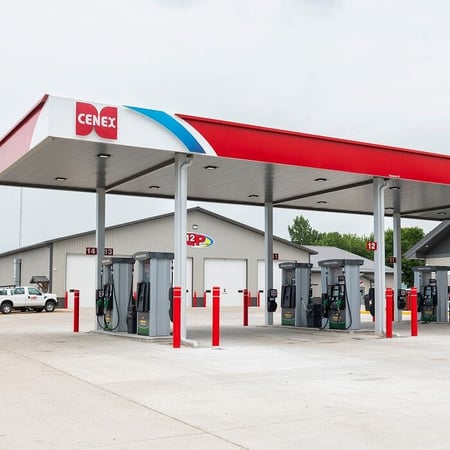Fuel station canopy covering multiple pump islands, with red bollards and service buildings in the background.