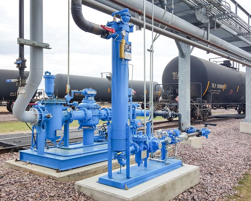 Blue blending skid at a rail terminal, with tank railcars on the tracks in the background.