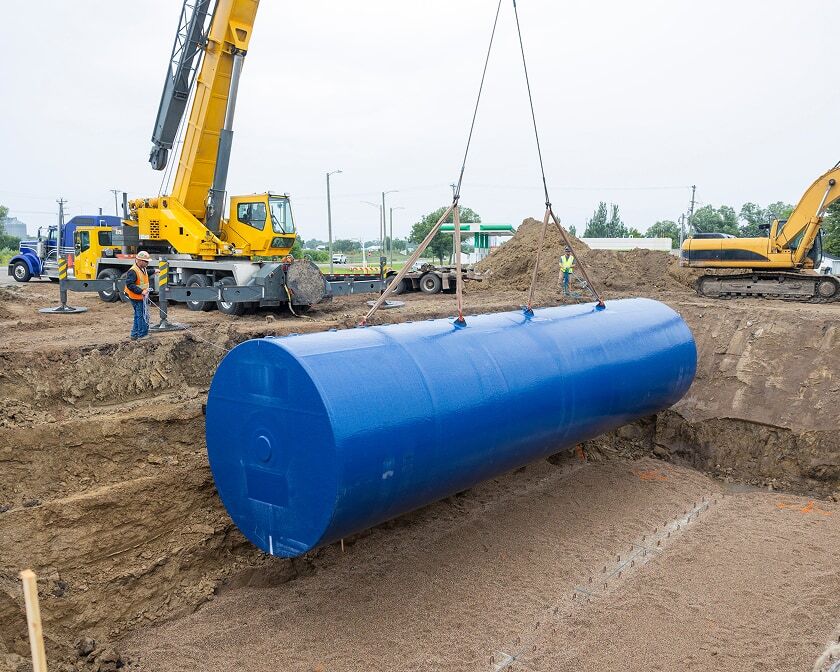 A large underground storage tank is suspended by lifting straps from a crane.