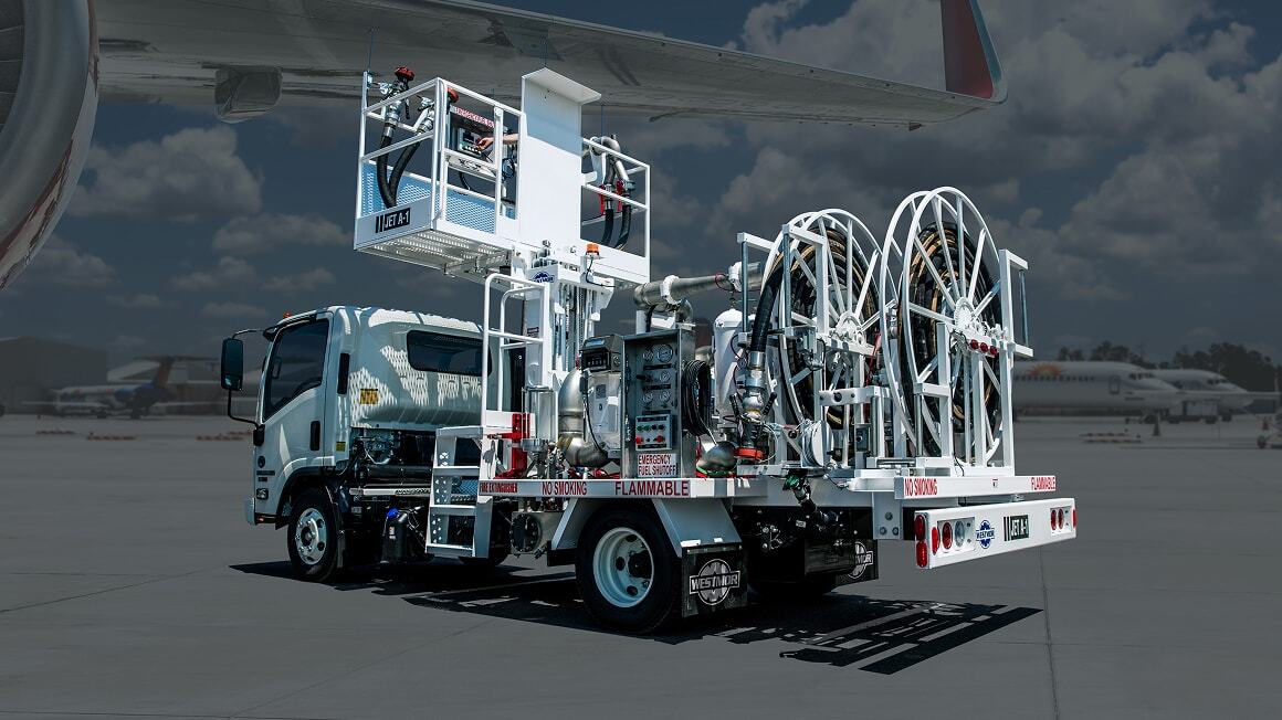 Aircraft refueling equipment with hose reels and fueling equipment parked on an airport ramp beneath an airplane wing.